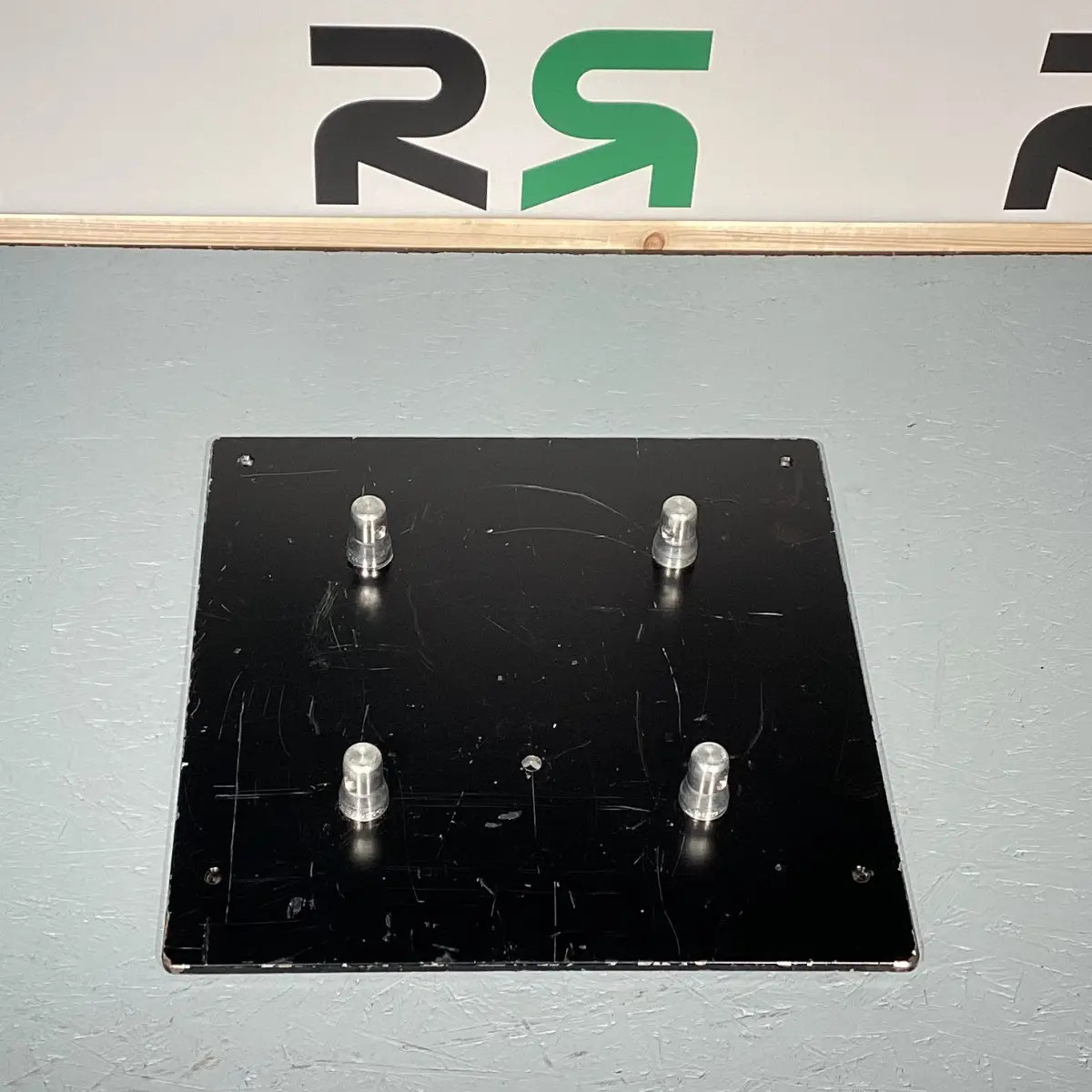 Montageplatte aus Syke mit vier stabilen Metallstiften auf grauem Untergrund: Praktisch und sicher für den flexiblen Event-Aufbau – jetzt ganz unkompliziert ausleihen!